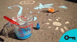 Des dessins de craie liquide sur du béton, avec un tasse à mesurer et des pinceaux.