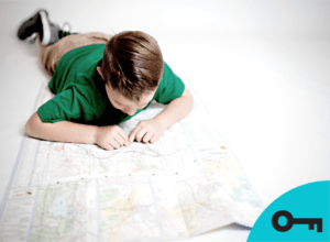 Un petit garçon couché sur une carte topographique l'inspecte avec son doigt.