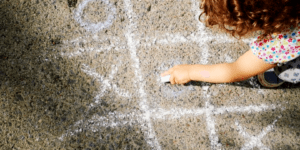 Une enfant trace un jeu de tic-tac-toe sur du béton.